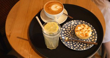 Krema ve limonata ile süslenmiş kahve kaplı kremalı turta tepside servis edilir. Lezzetli organik içecekler ve küçük kafe masasında sağlıklı bir tatlı. Basit bir yemek.