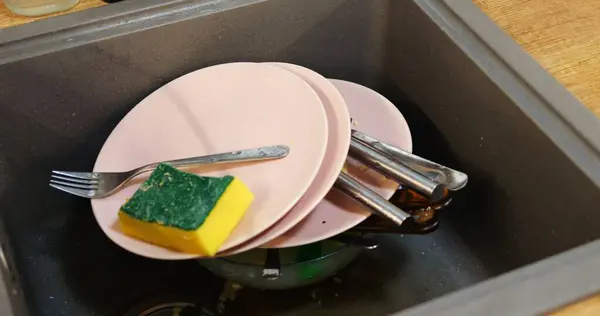 Mutfak lavabosuna konmuş kirli bulaşıklar ve tıkanmış atık süzgecinde yemek artıkları. Yemeklerden sonra temizlik görevi, temizliği korumak için zamanında eylem gerektirir