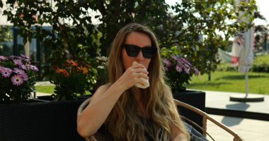 Uzun saçlı bir kadın çalıların gölgelediği kafede tavuk sarması yiyor. Fast food popülerlik konsepti. Çalışırken yüksek kalorili atıştırmalıklar.