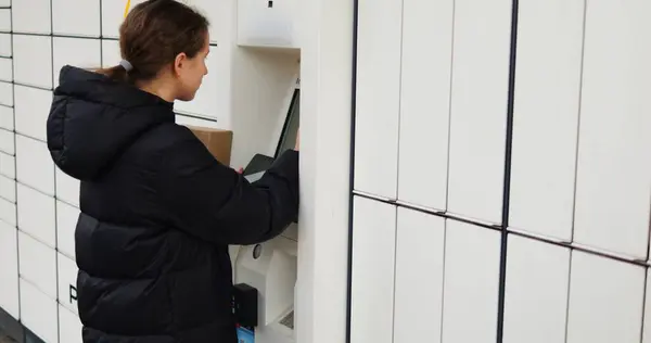 Genç kadın otomatik parsel terminalinin dokunmatik ekranından bilgi giriyor. Esmer kadın paket göndermeye hazırlanan sevkiyat detaylarını giriyor.