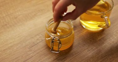 Kadınlar bardaktaki limon çayını dengelemek için cam kavanozda bal çırpıyor. Doğal tatlandırıcı ile zenginleştirilmiş ılık içecek sindirimi destekler.