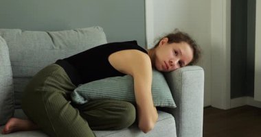 Cesareti kırılmış genç kız kanepede uzanmış yastığa sarılıyor ve üzgün gözlerini açıyor. Kız arkadaşlarıyla yanlış anlaşılma yüzünden olumsuz duygular yaşıyor.