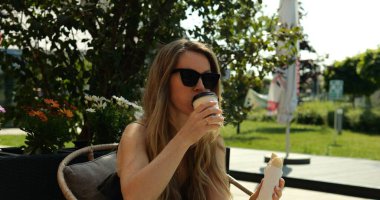 Bayan kafe ziyaretçisi parkta yaz terasında hamur işleriyle servis edilen kahveyi rahatça içiyor. İş kadını molada sokak kafesinde öğle yemeği yiyor.