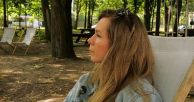 Sarı saçlı bayan parkta doğayla baş başa kalmaktan hoşlanıyor. Kadın, kamuya açık bahçenin gölgeli bir köşesinde güneşlenerek rahatlıyor.