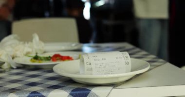 Tabak fiyatları ve toplam miktarı olan kağıt fatura kantindeki müşterilere karşı tabağa konuyor. Son miktara sahip ince kontrol sosyal etkinliğin sonunu simgeler