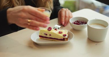 10 Mart 2023 'te kadın kafe masasında oturan böğürtlenli peynirli kekin üzerine sos döküyor. Bayan kahveyle yemeden önce ekstra şefkat için tatlıya kremalı sos ekliyor.