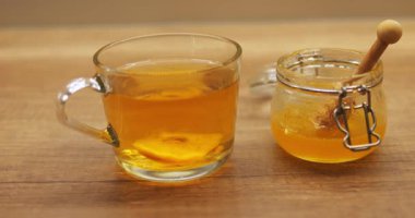 Kavanozdan bal karıştırılmış şeffaf fincanda limon dilimleri kes. Doğal tatlandırıcılı sıcak içecek grip sırasında boğaz ağrısını dindirir.