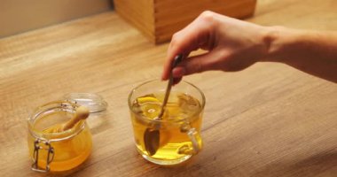 Kadın eli sıcak çayı limonla karıştırıyor ve cam bardakta bal sakinleştirici bir içecek oluşturuyor. Citrus dilimleri kaynar suda kıvrılır ve ferahlatıcı bir tat yaratır.