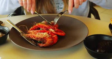 Kadınlar küçük yuvarlak masada oturan büyük karidesler için çatal ve bıçak kullanır. Bayan, tropikal tatil köyündeki kafede boş vakit geçirir ve özel deniz mahsullerinin tadına bakar.