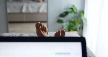 Dizüstü bilgisayarı açık Freelancer yatakta uzanıp yatak odasındaki web projesinde çalışıyor. İnsan şakacı hareketlerle iş için rahat ortamlardan keyif alır.