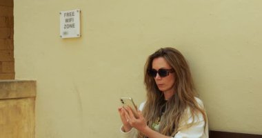 Olgun bayan bilgi aramak için halka açık yerlerde internet teknolojisi kullanıyor. Kadın terminaldeki bankta oturuyor ve modern akıllı telefonun ekranına dokunuyor.