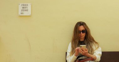 Kadın koridorda bankta oturuyor ve bedava Wi-Fi bölgesindeki akıllı telefon ekranına dokunuyor. Bayan, uçağın terminalden kalkmasını bekleyen bir aletle çalışıyor.