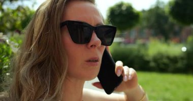 Endişeli kadın telefonu kulağına tutuyor güneş gözlüğünü ayarlıyor ve arkadaşıyla konuşuyor. Bayan, dışarıda anons sırasında huzursuz ve düşünceli bir ilişki yaşıyor.