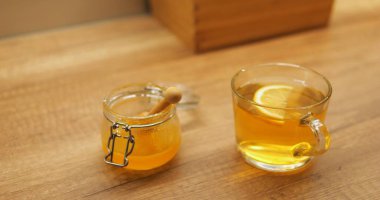 Canlı limon dilimleri bal kavanozunun yakınındaki ahşap yüzeye yerleştirilmiş aromatik çay bardağında döner. Sakinleştirici içecek bunaltıcı günlerde gevşemeyi teşvik eder.