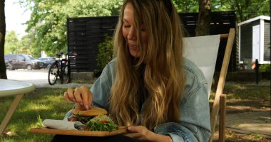 Kadın ana yemek olarak sunulan salata yaprağını ağzına koyar. Hamburgerin besinlerini dengelemek için hamburgerle servis edilen yeşil garnitür