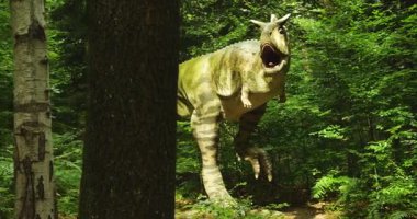 Karnotaur yeşil dinozor modeli, canlı orman ortamında duran büyük ağaç gövdesi ile gizlenmiş. Model açık ağız ve boy doğal çevreye dramatik bir unsur ekler