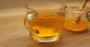 Tahta masada şeffaf bardakta dönen limon dilimli sıcak çay. Bal kavanozunda bal, ballı tatlandırıcı. Sıcak içecek, doğal tatlılık.