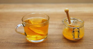 Ahşap yüzeyde bal kavanozunun yanında limon dilimli cam bardak demleme çayı. Tatlı ve ekşi aromalı taze bir içecek.