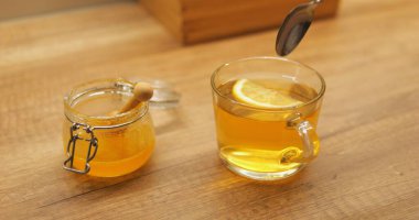 Kadın taze limon ve bal kokulu çayı karıştırıyor cam bardaktaki tatları birleştiriyor. Sıcak içecek soğuk kış günlerinde enerji seviyelerini canlandırır.