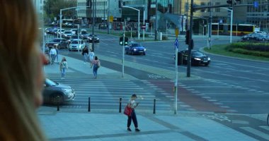 Kadın, yayalar ve araçlarla dolu şehir kavşağında camdan dışarı bakıyor. İnsanlar modern şehir ortamında trafik ışıklarında bekliyor.
