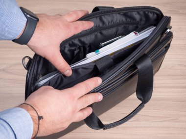 Bir adam beyaz arka planda siyah deri bir evrak çantası açıyor.