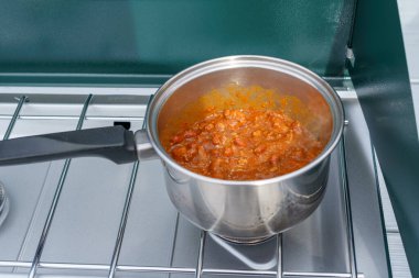 Açık hava propan kamp sobasında gümüş bir tencerede kırmızı biber pişirmek.