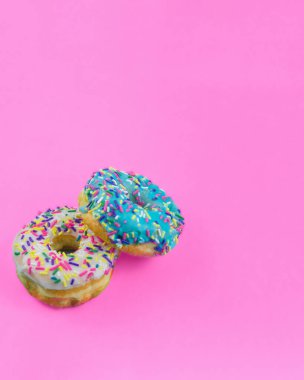 Mavi ve beyaz kremalı iki donut ve parlak pembe bir zemin üzerinde parlak pembe serpiştirilmiş fotokopi alanı için yer var..