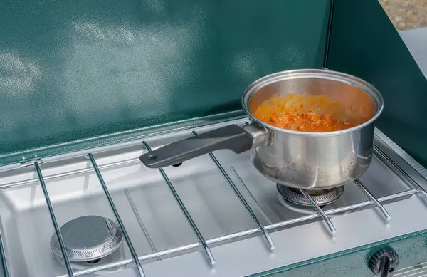 Cooking chili in a silver pot on a green outdoor propane camp stove