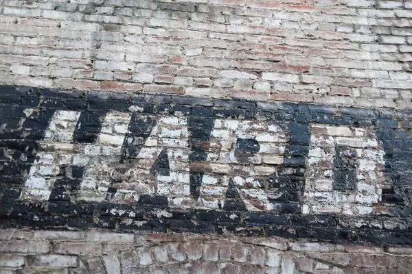 The word HARD is painted with black and white paint on an old, weathered brick wall. The ghost sign is distressed with a lot of texture.