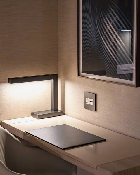 Masa lambasından karamsar ışıklar çıkan modern bir otel odasında çalışma masası.