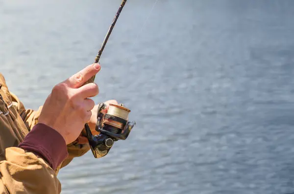 Close-up of a young man reeling in with an old fishing rod and reel at a lake. Room for copy space.