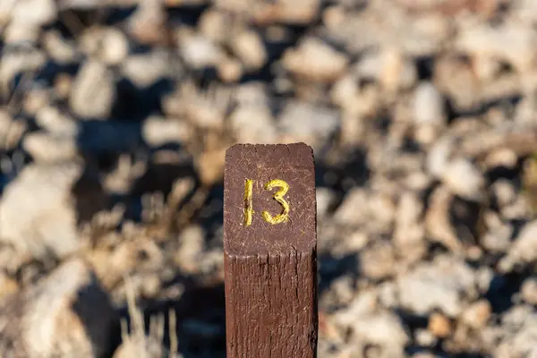 Trail Mile Marker Number Thirteen (13) carved on a wooden post and painted yellow
