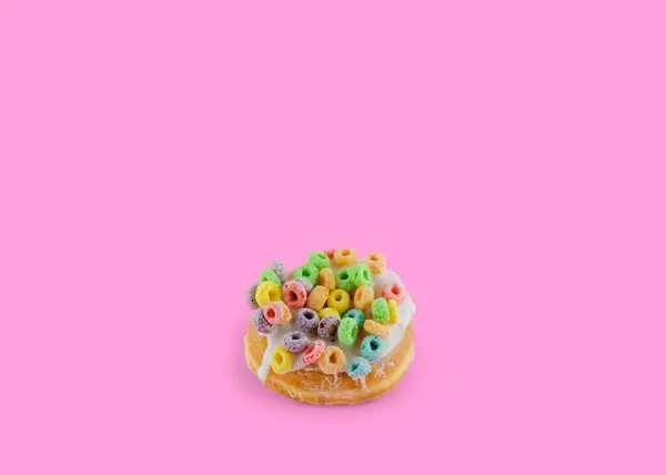 Pink donut with colorful loop cereal on a pink background with copy space