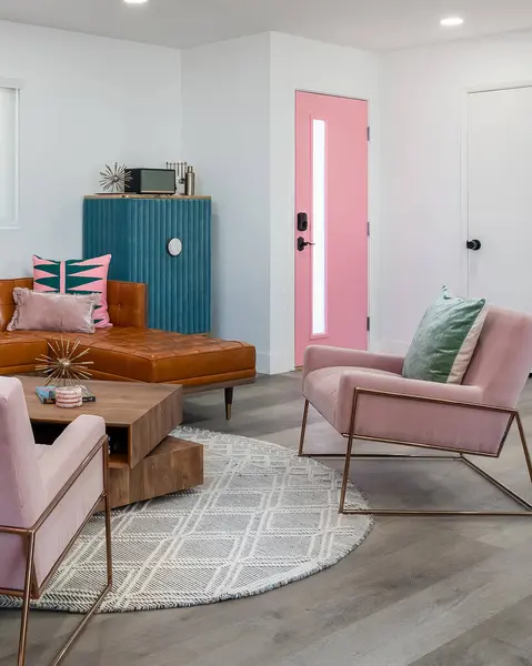 Trendy mid-century modern living room with pink chairs, a pink door, and leather sofa.