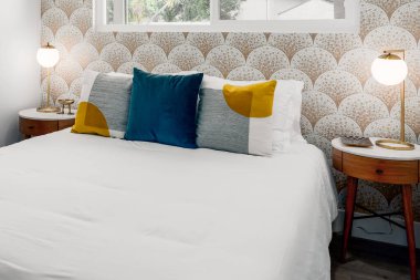 Rahat yatağı, yastıkları, komodinleri ve mozaik duvar kağıtları olan modern misafir odası.