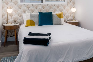 Rahat yatağı, yastıkları, komodinleri ve mozaik duvar kağıtları olan modern misafir odası.