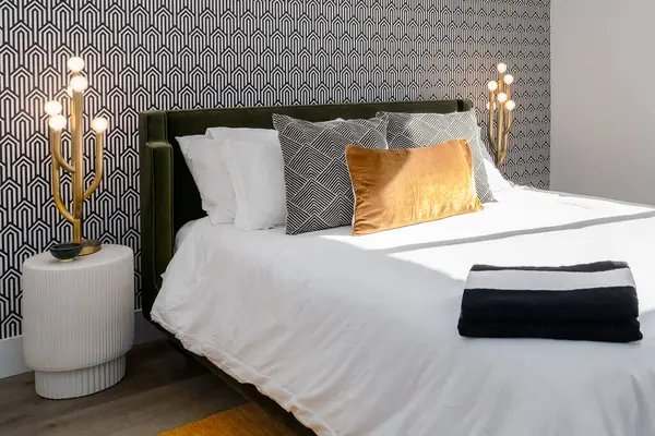 Luxurious black and white bedroom with gold lamps, gold pillow, and cool wallpaper