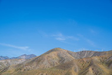 Cabazon yel değirmenleri San Gorgonio 'nun tepesinde mavi gökyüzü ve kopyalama alanı olan dağları geçiyor.