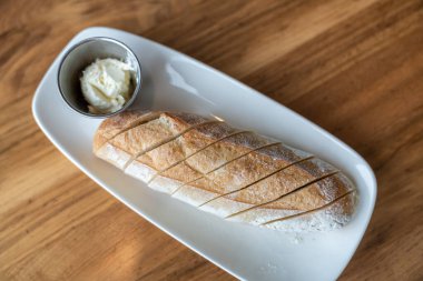 Beyaz bir tabak üzerinde tereyağı ve ahşap masa ile ekmek ekmeğinin üst manzarası