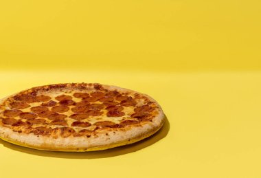 Merkezin solundaki biberli pizza sarı arka plandaki stüdyoda fotokopi alanı ile çekiliyor.