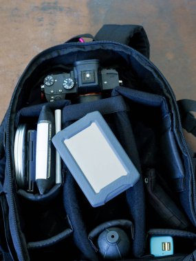 Kamera, lens, hard disk ve diğer aksesuarlar dahil olmak üzere fotoğraf ekipmanlarıyla dolu açık siyah bir kamera çantası. Kamera üst kompartımanda görünüyor..