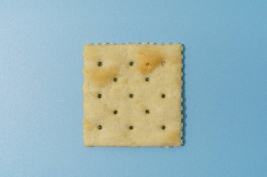 Tek kare tuzlu kraker, desenli bir yüzeyi ve küçük delikleri var, mavi bir arka planda..