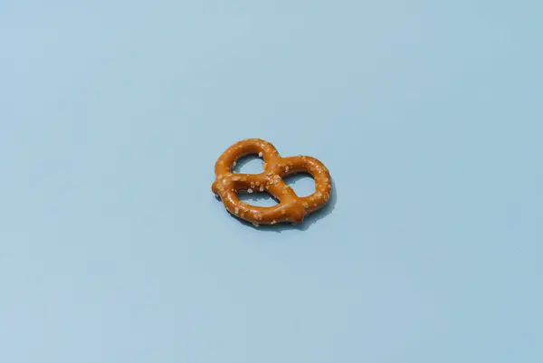 Tuz kristalli tek bir kahverengi çubuk kraker mavi arka planda duruyor. Pretzel odak noktasında, arka plan ise biraz bulanık. Işıklandırma yumuşak ve doğal..