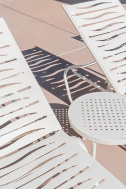 Güneşli bir günde gölgeli havuz terasında masalı beyaz şezlonglar ve el sallama desenleri. Sandalyeler desenli gölgeler bıraktı.