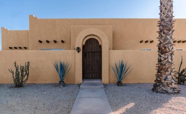 Adobe Güneybatı Pueblo tarzı mimarlık. Amerikan Çölü 'nde kaktüs ve palmiye ağacı olan bir ev.