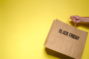 Kara Cuma kahverengi kağıt alışveriş torbası, bir erkeğin elinde, sarı arka planda, fotokopi alanı olan bir erkek tarafından tutuluyor..