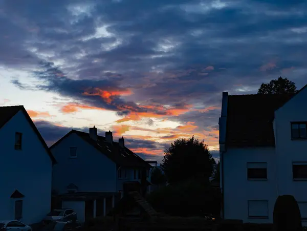 The evening sky is covered with red clouds on a summer evening in a European small town. Picturesque sunset and silhouettes of houses and trees