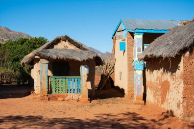 Madagaskar 'daki Malagasy köyü. Arka planda mavi gökyüzü olan sazdan çatılı üç turuncu tuğla kulübe. Zavallı Afrika köyü. Zavallı Madagaskar evleri.
