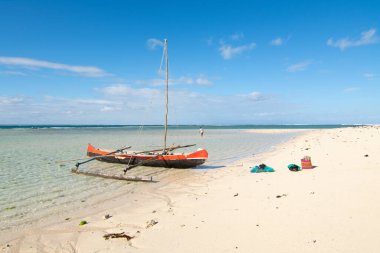 Pirogue teknesiyle Anakao, Madagaskar 'daki Meraklı ve Adası' na. Arka planda mavi gökyüzü olan beyaz bir kumsal üzerindeki bir pirogue tekne görüntüsü.