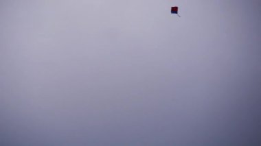 Kırmızı ve mavi bir uçurtma, beyaz bir gökyüzünde yavaşça aşağı ve yukarı uçuyor. Uçurtmanın yakın çekim görüntüsü..